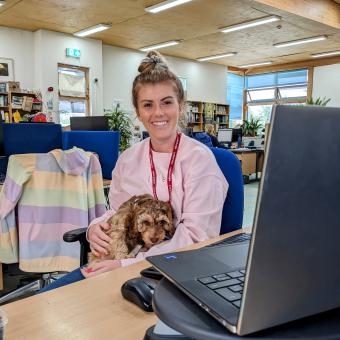 Office team member sat with puppy at desk with laptop